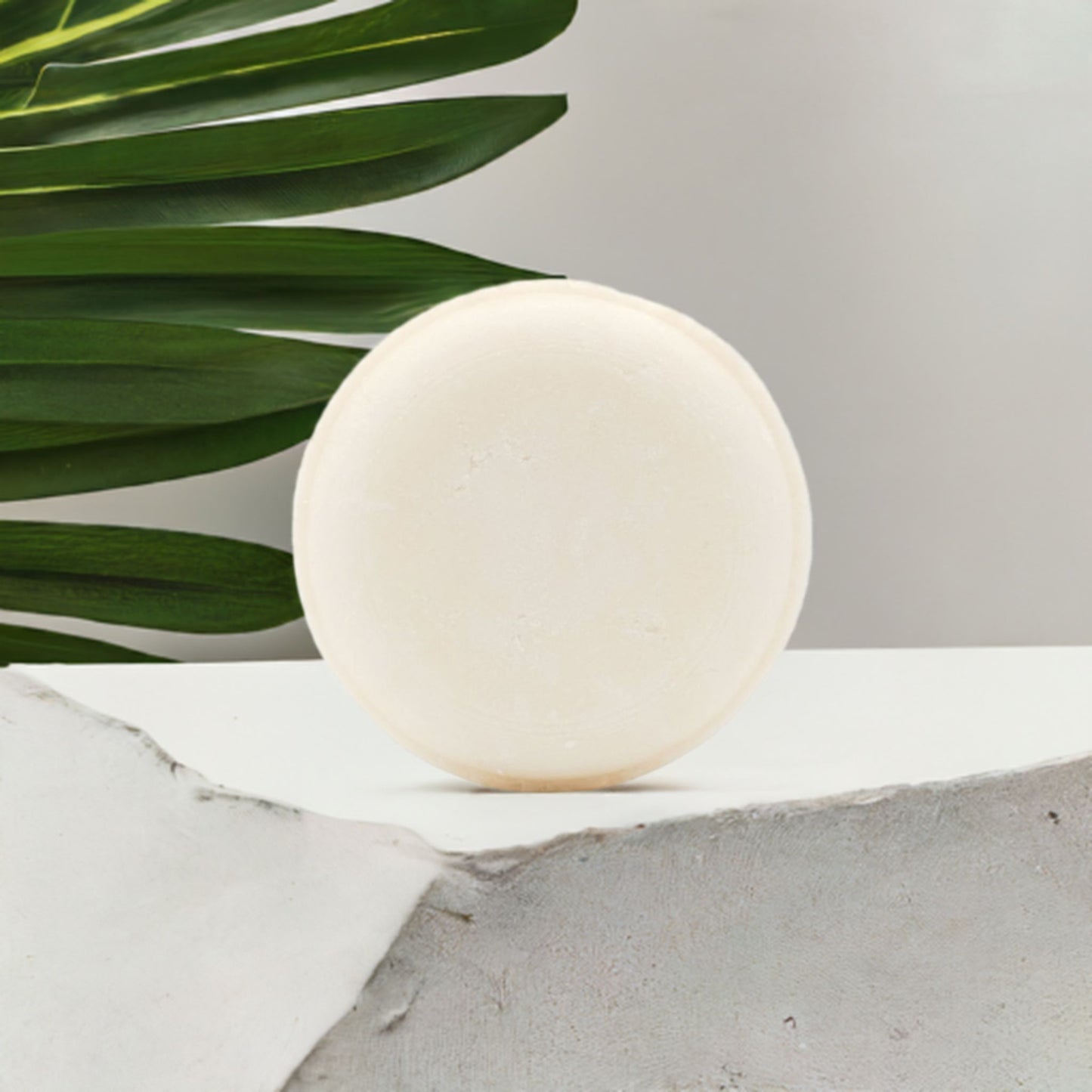 White shampoo bar on a gray surface with green leaves in the background