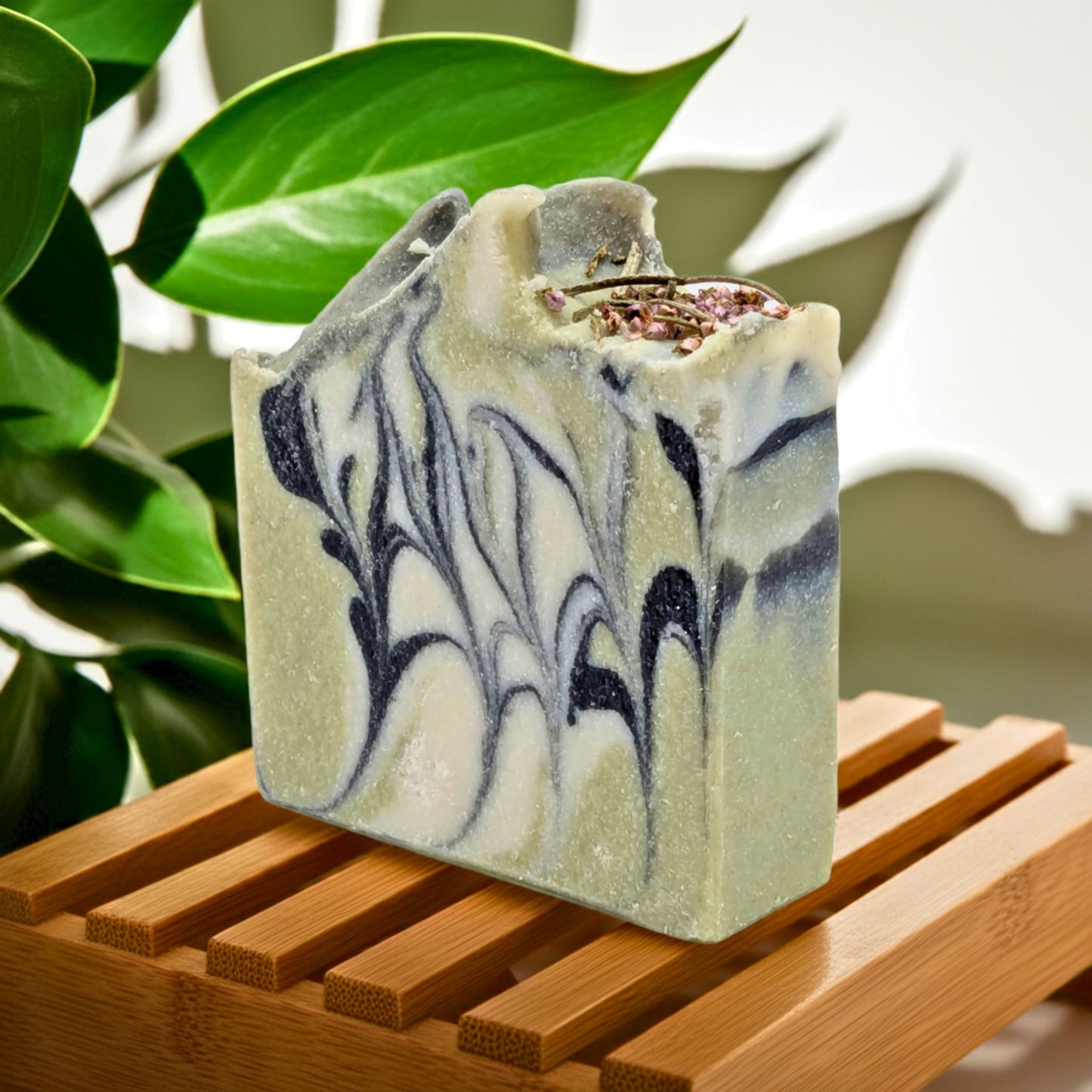Marble-patterned soap bar on a wooden surface with green leaves in the background