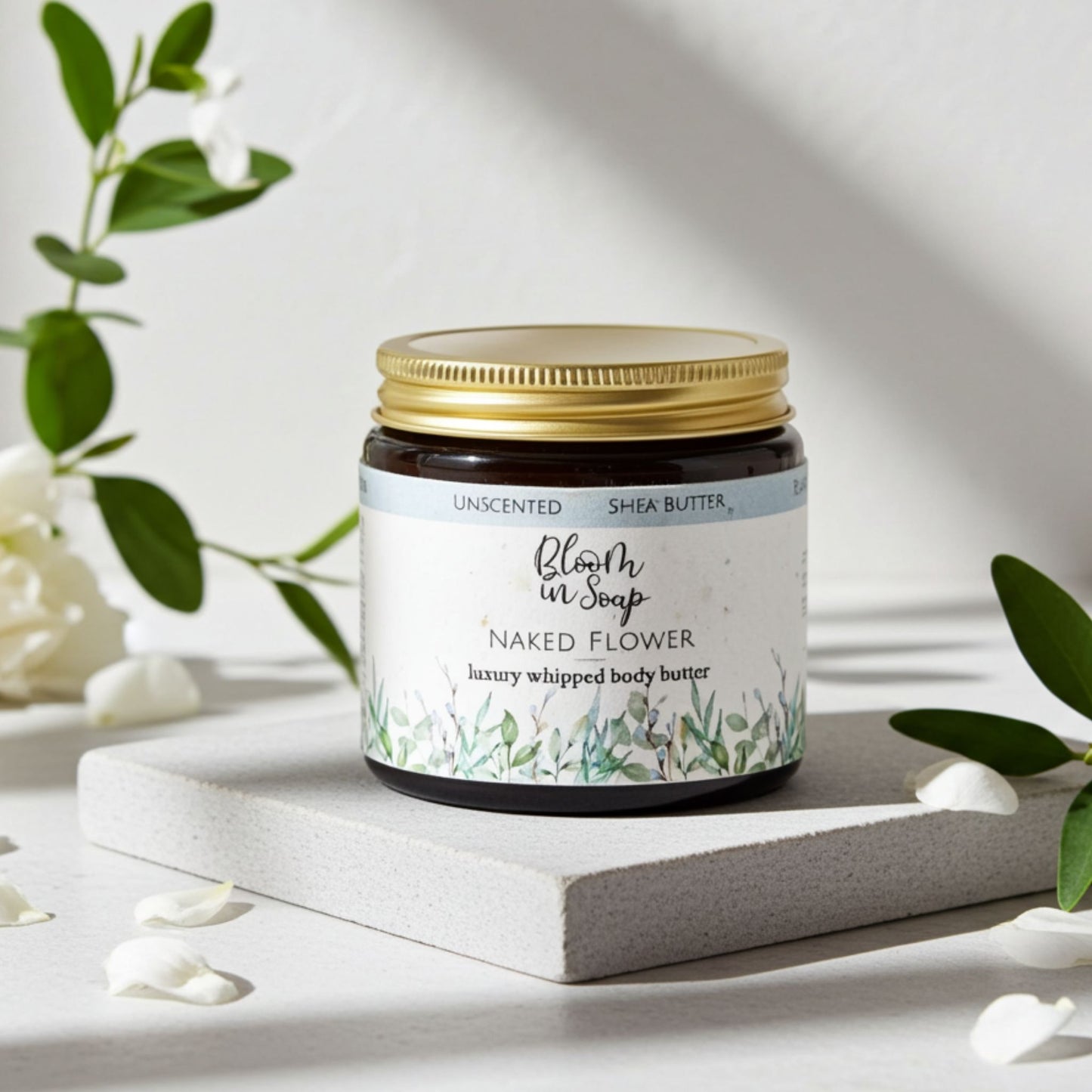 jar of Naked Flower body butter with petals and greenery in the background