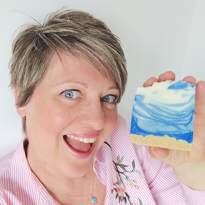 a woman smiling and holding a bar of natural soap