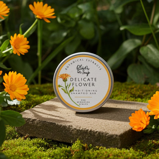 Shampoo bar tin on a stone platform with calendula flowers and greenery
