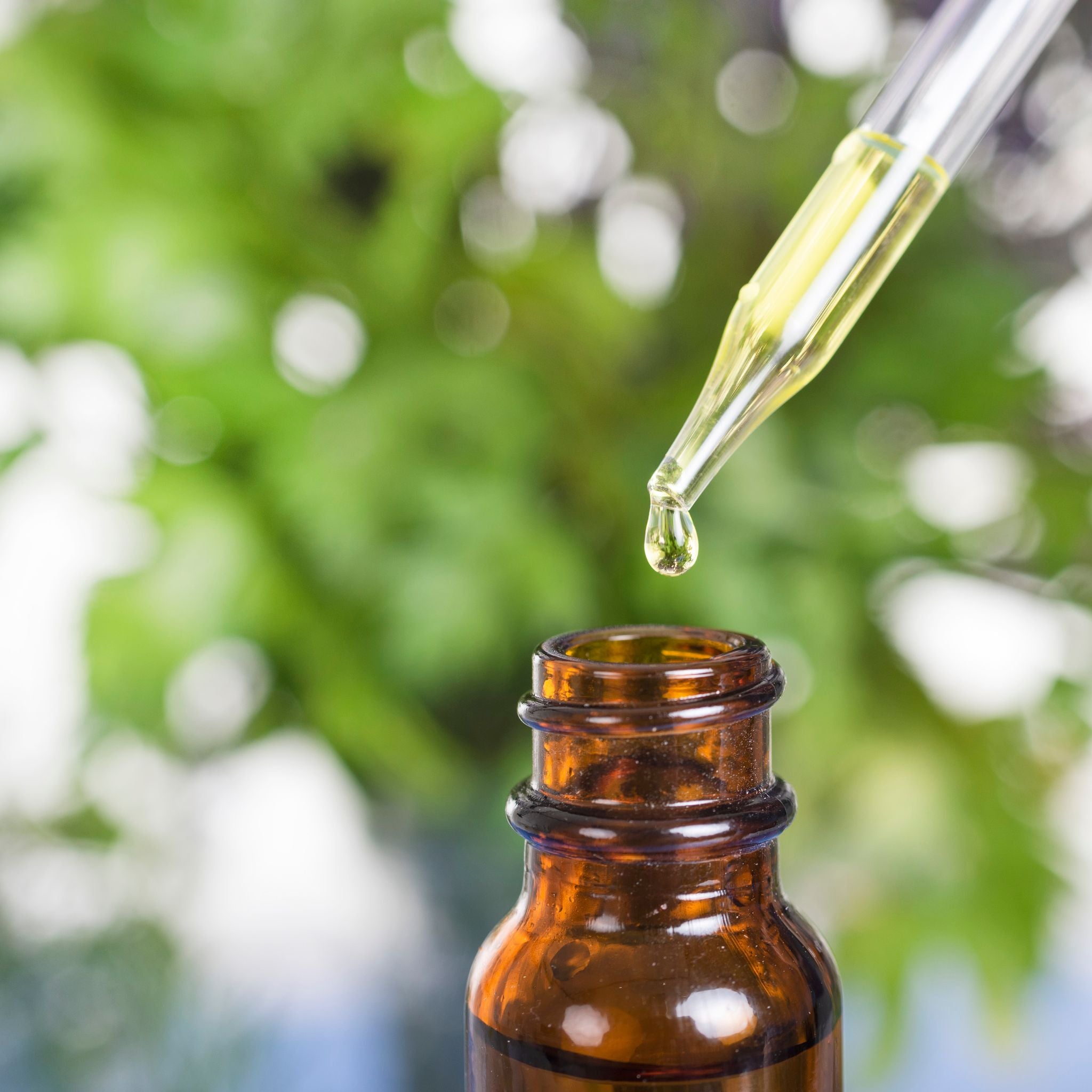 Amber glass bottle with dropper  of essential oil against a blurred green natural background