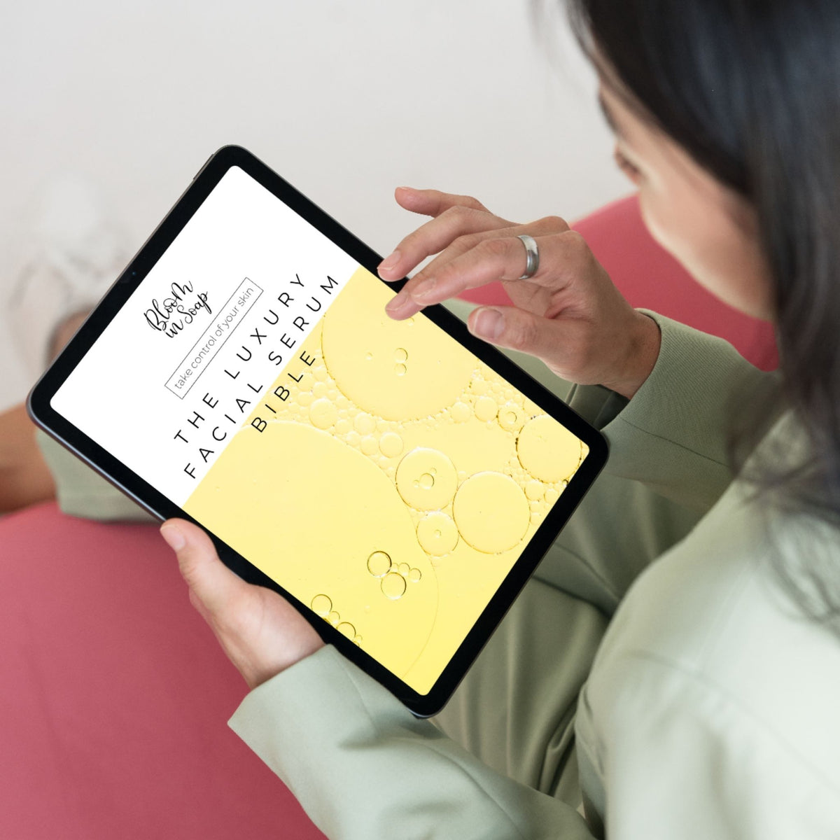 A woman holds a tablet showing a digital cover for 'The Luxury Facial Serum Bible' by Esthetic Journey. The cover features a yellow background with 3D bubble graphics.