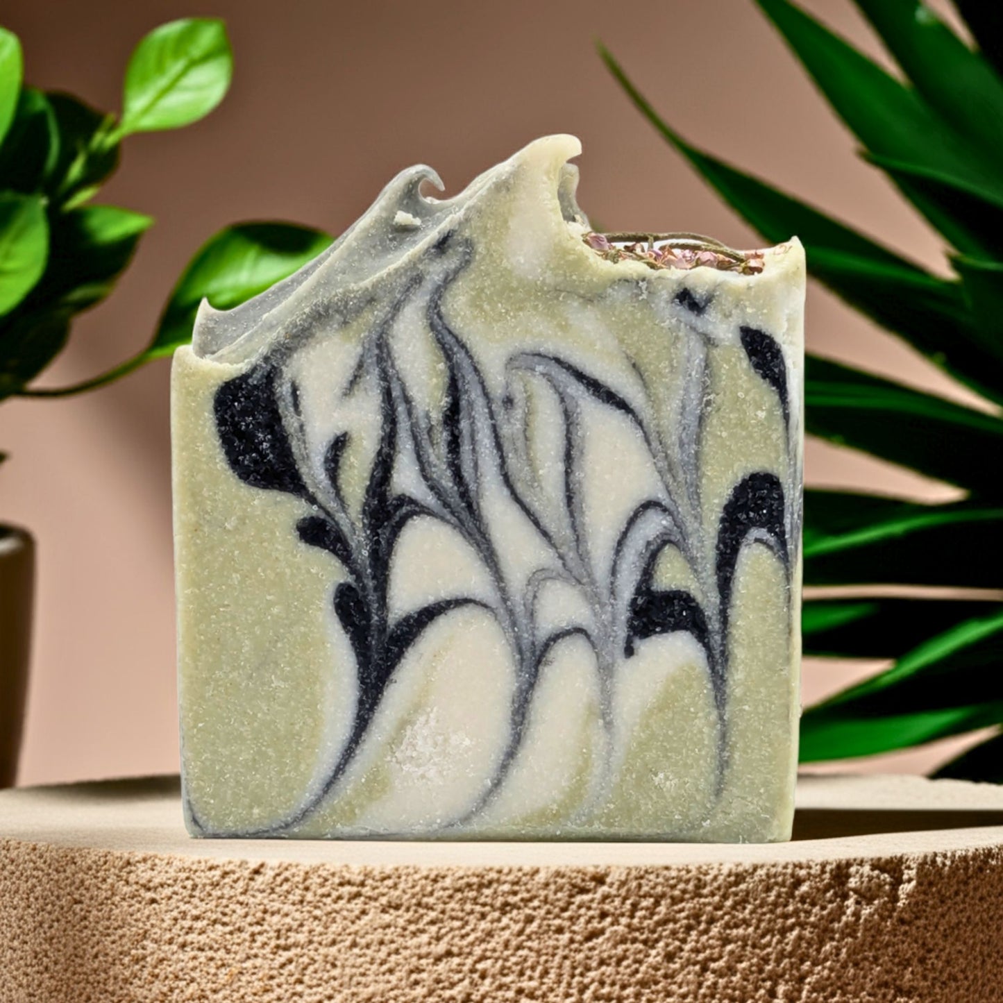 Marbled green and black soap bar on a textured surface with plants in the background