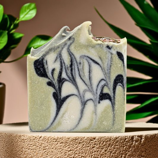 Marbled green and black soap bar on a textured surface with plants in the background