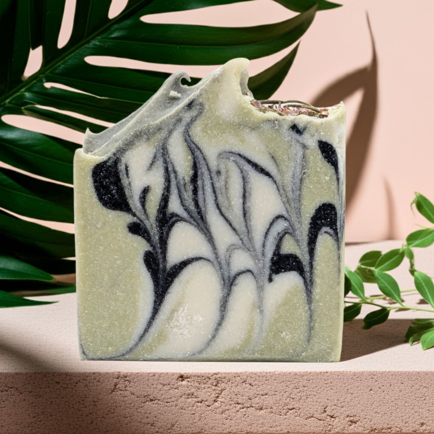 Marble-patterned soap bar with green and black swirls on a pink background with leaves.