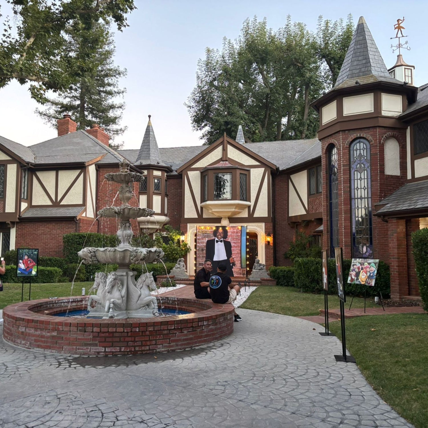 Fountain in front of a large, ornate house with a clock tower.
