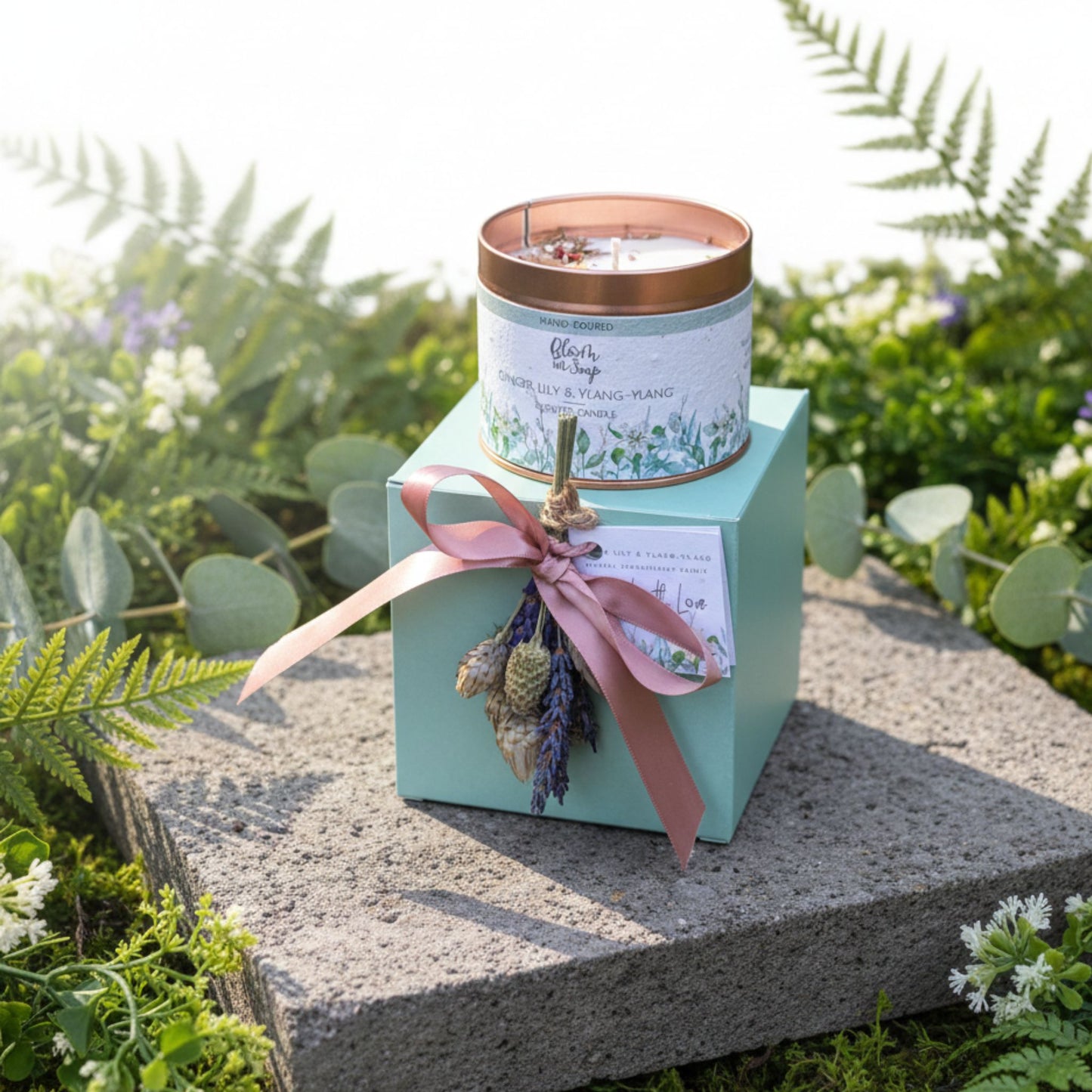 Candle in a tin with decorative elements on a stone surface surrounded by greenery