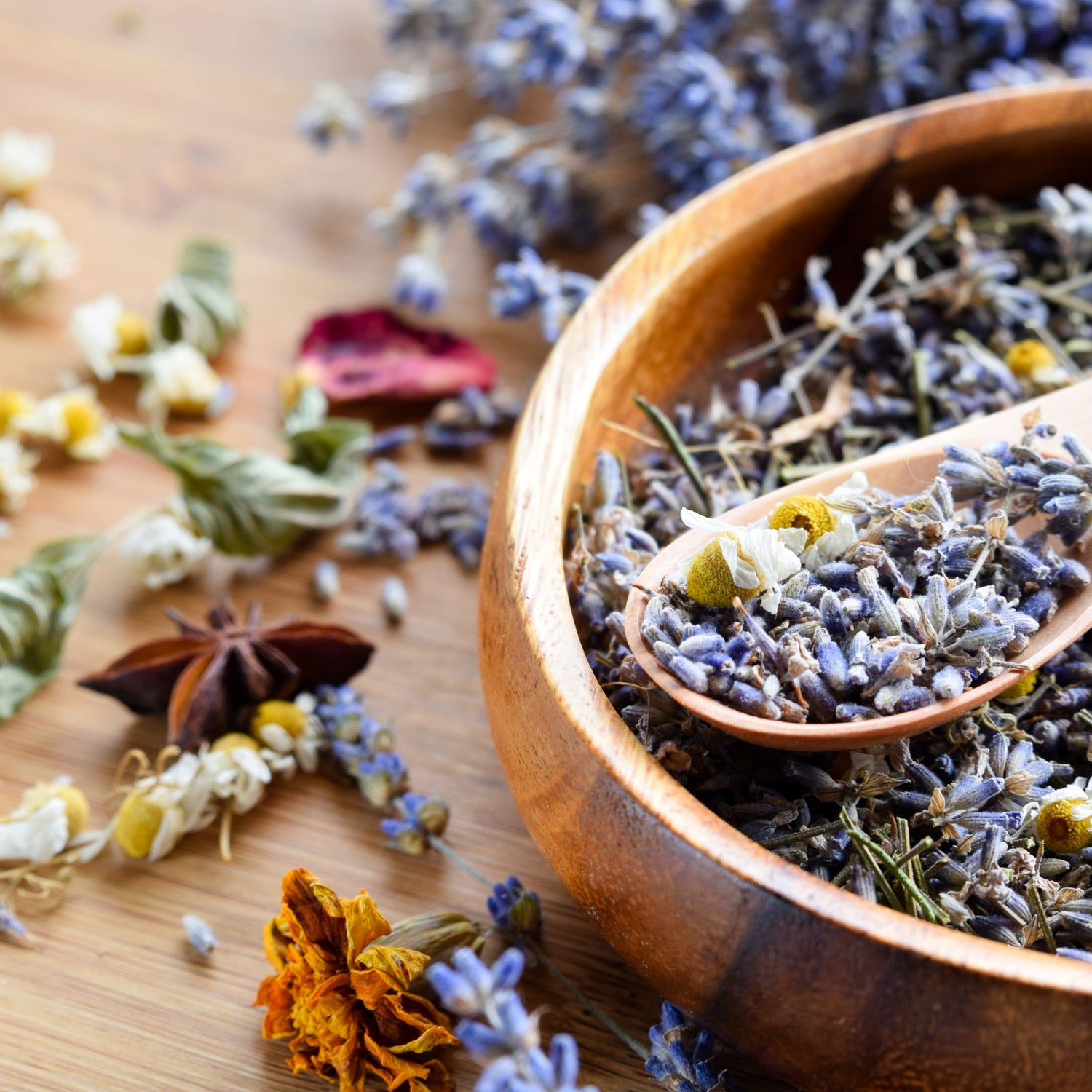 Wooden bowl filled with dried lavender flowers on a wooden surface.