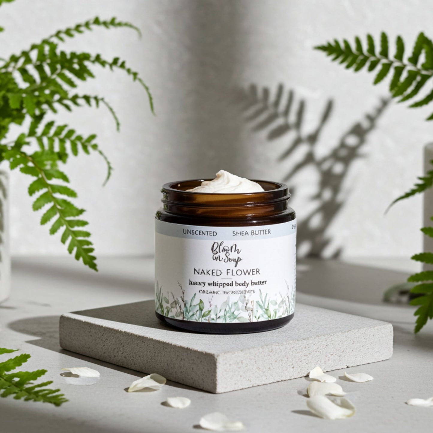 open jar of body butter with petals and greenery in the background