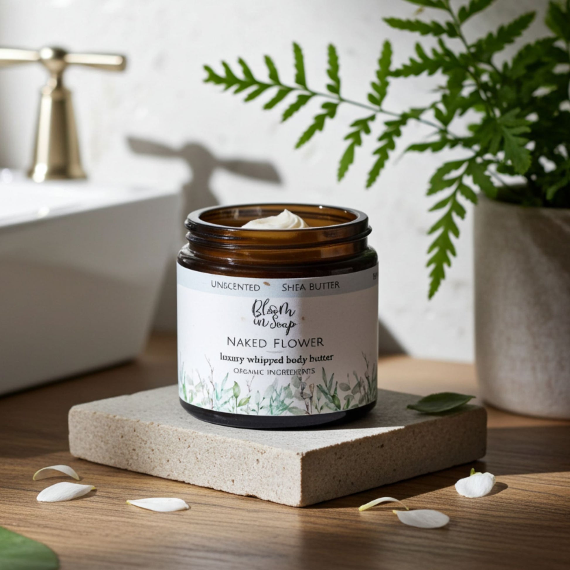 jar of body butter with petals and greenery in the background in a bathroom setting