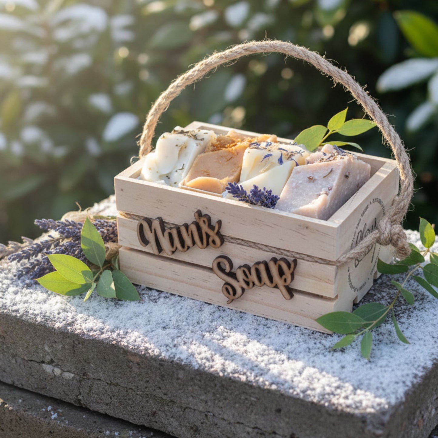 Wooden box with 'Nan's Soap' branding containing various soaps, surrounded by greenery.