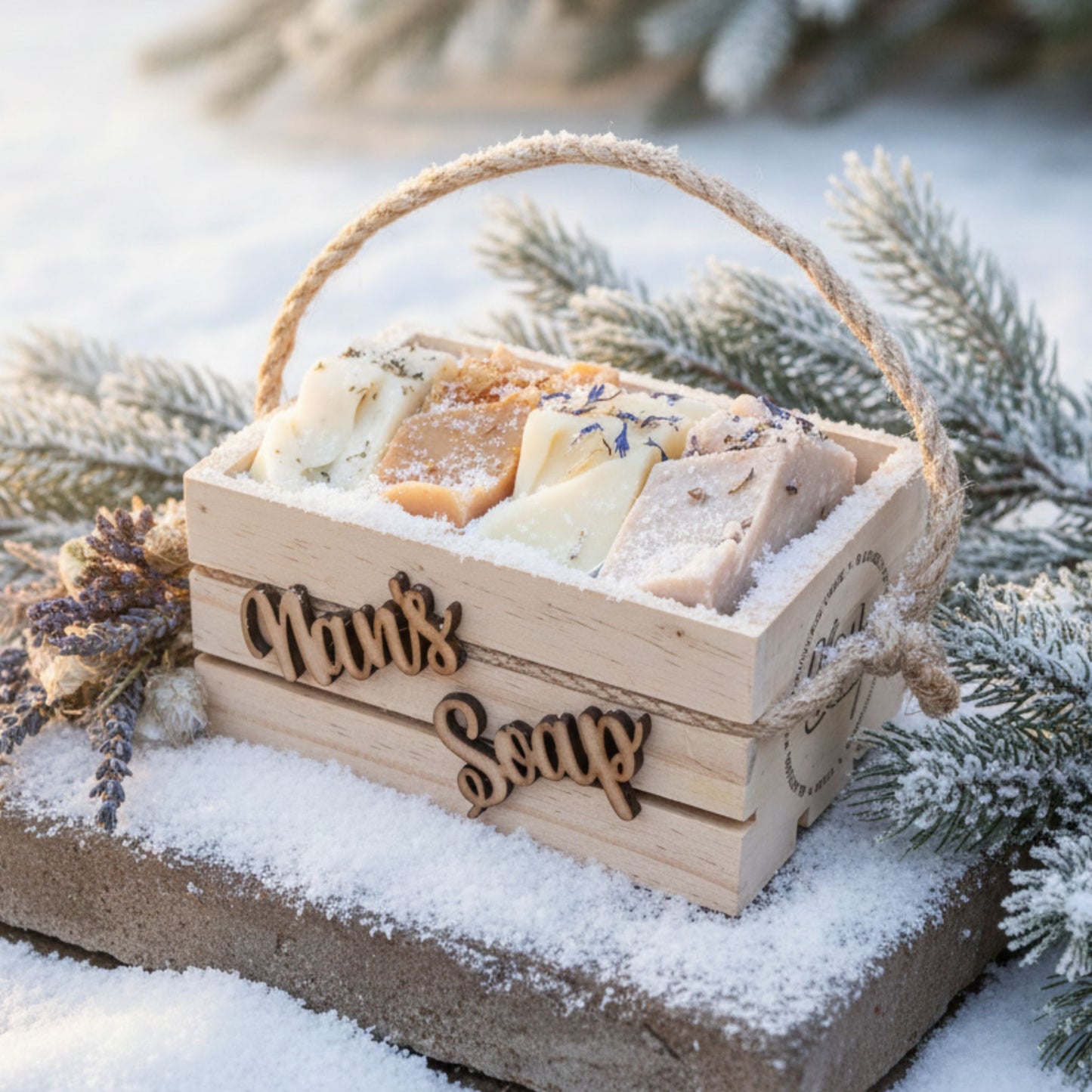 Wooden box of soap with 'Nan's Soap' engraved, surrounded by snow and evergreen branches.