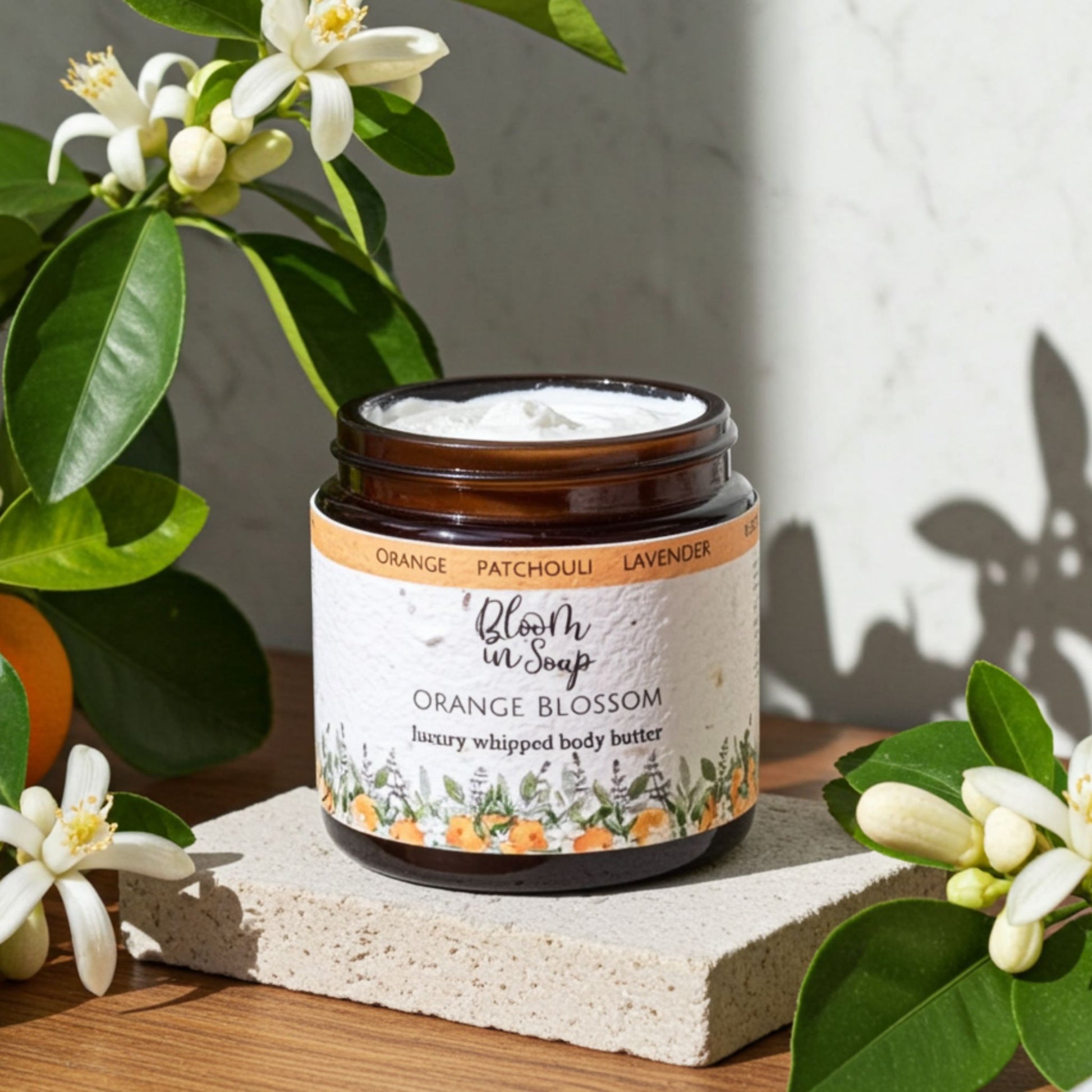 JAr of Orange Blossom body butter on a stone with orasnge blossom