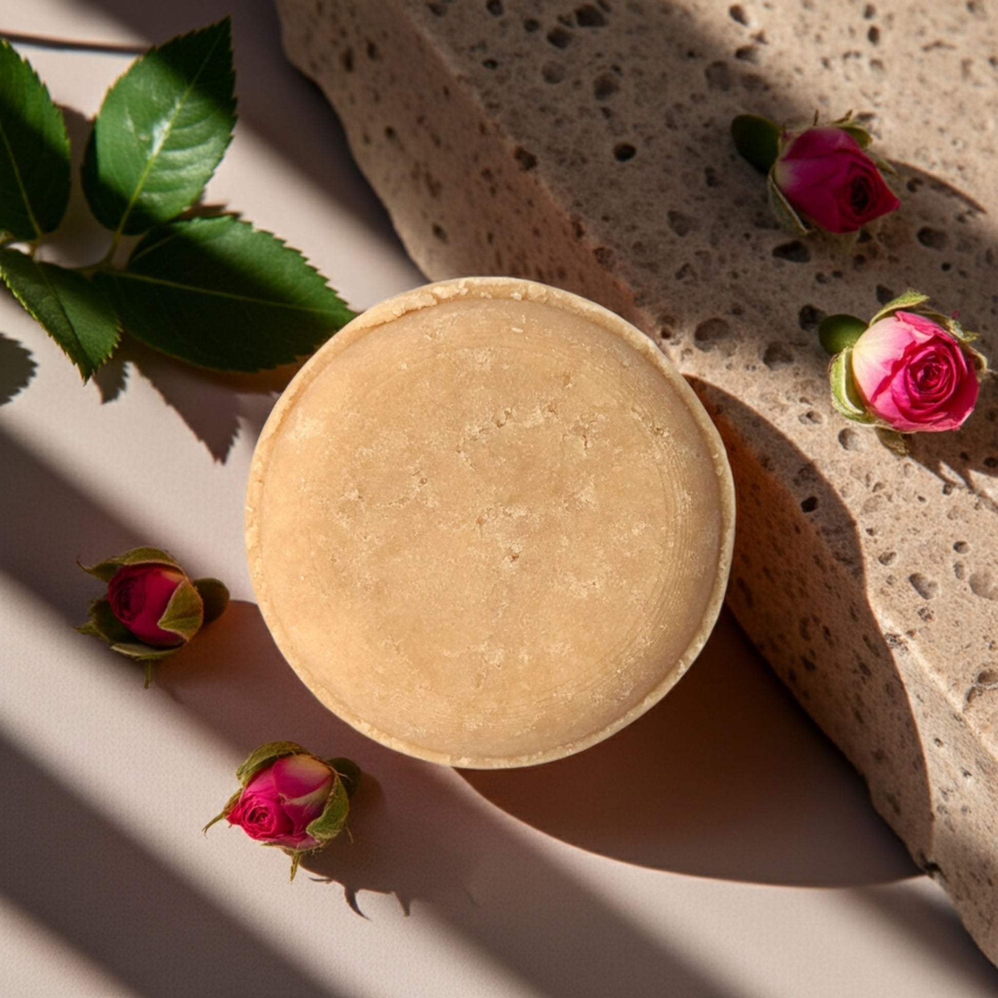 Round pink shampoo bar and roses on a light surface