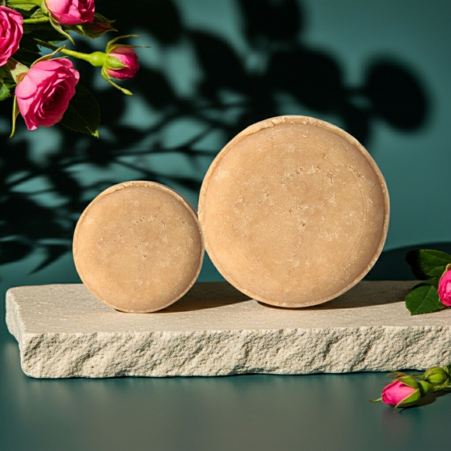 Two round pink shampoo bars on a stone platform with pink roses in the background.