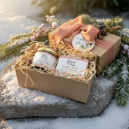 Gift basket with a body butter jar, soap, and other items on a snowy surface with evergreen branches.