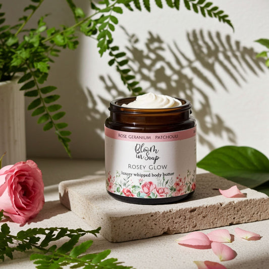 Jar of body butter with floral label on a stone surface with pink roses and green leaves.