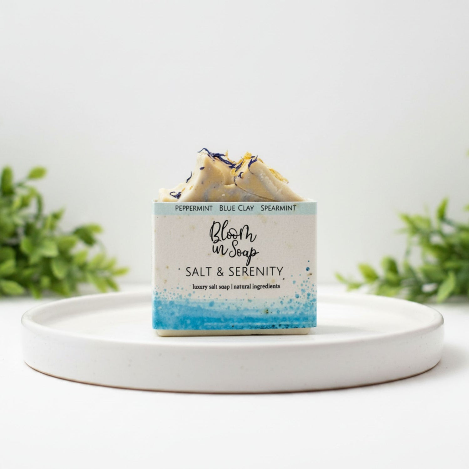 Bar of soap with a label on a white plate, surrounded by greenery