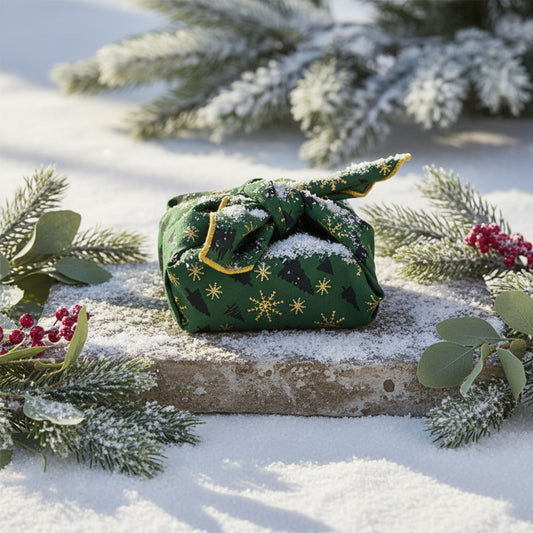 Green fabric gift furoshiki with gold patterns on a snowy surface with evergreen branches.