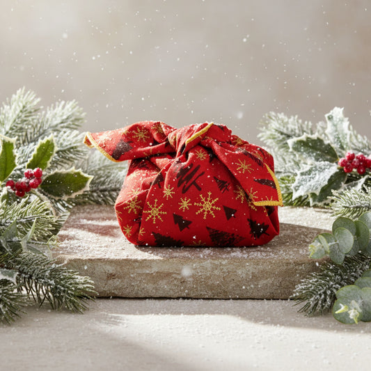 Red fabric furoshiki with Christmas patterns on a snowy surface with greenery