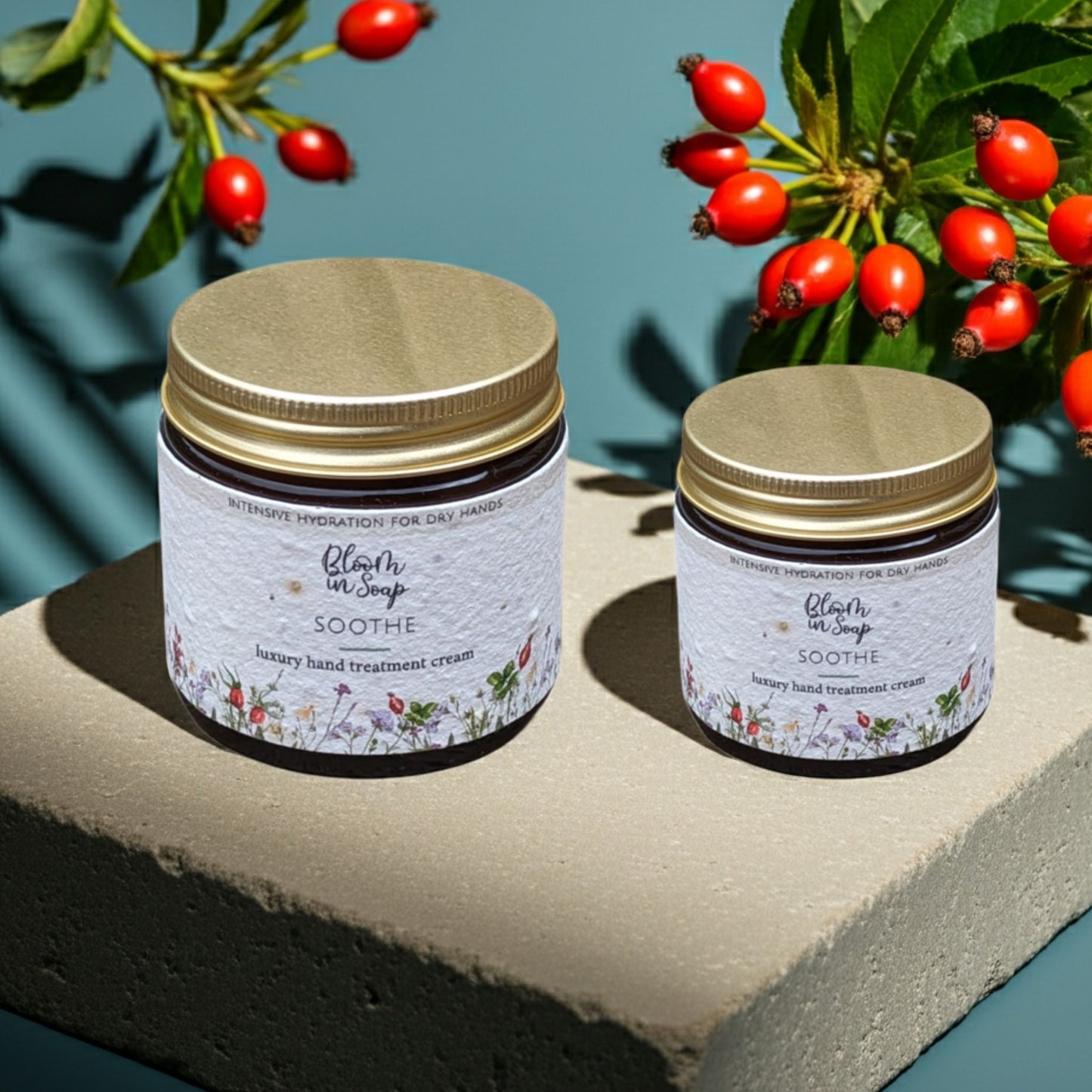 two jars of soothe hand cream on a stone with a blue background and rosehips in the background