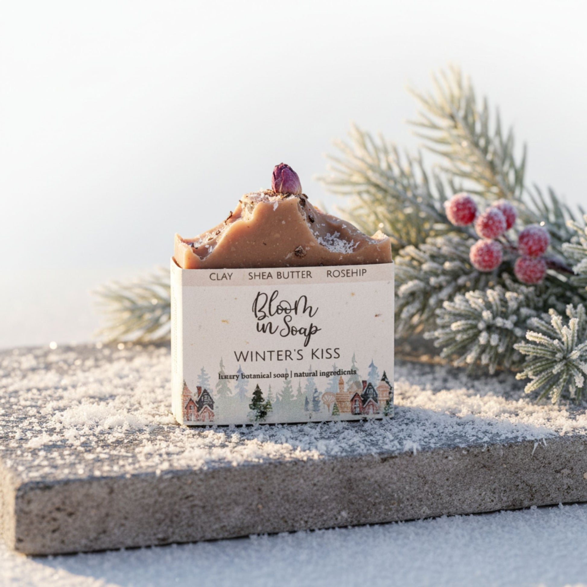 Bar of soap with a decorative box labeled 'Winter's Kiss' on a snowy surface with evergreen branches.
