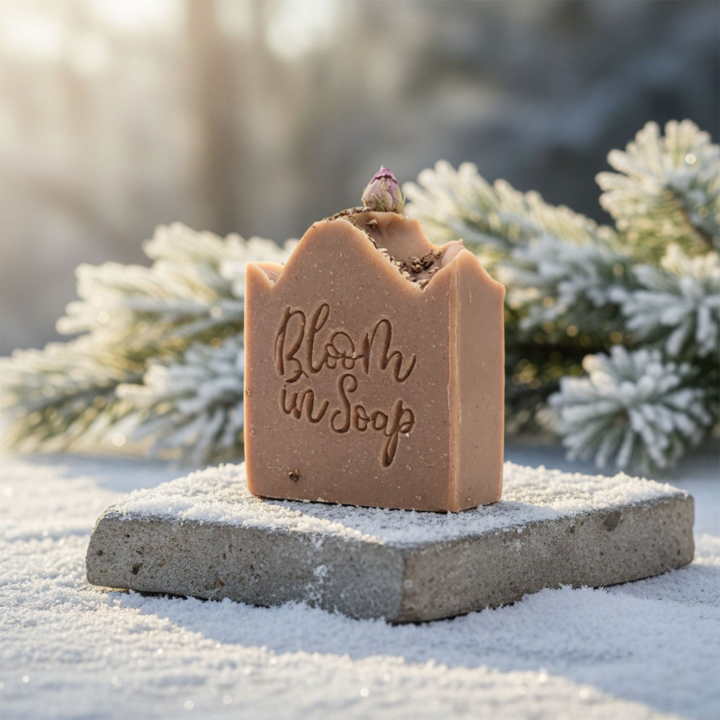 Bar of soap with 'Bloom in Soap' text on a stone block in a snowy landscape.