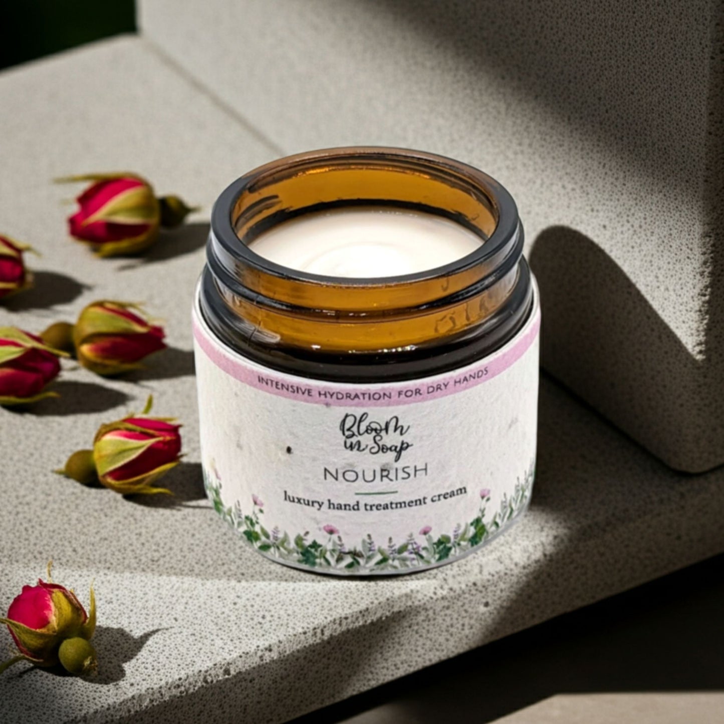 Jar of hand treatment cream with dried roses on a stone surface