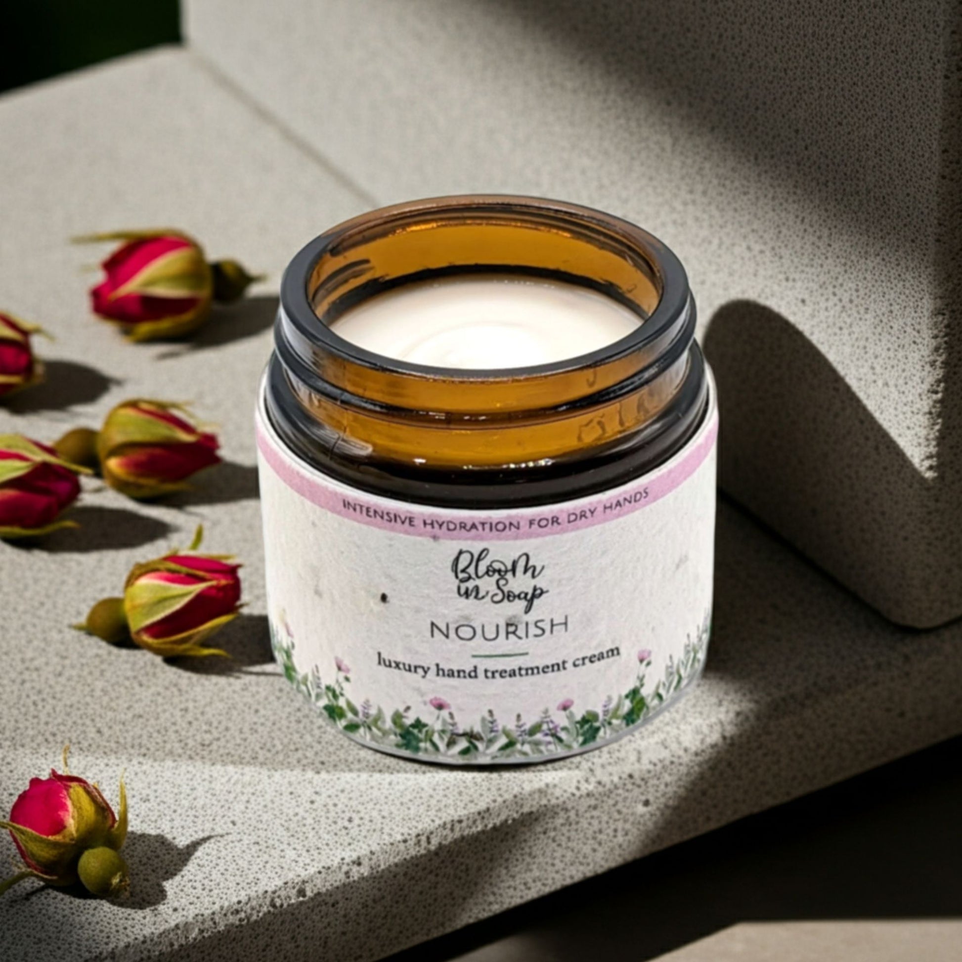 Jar of hand treatment cream with dried roses on a stone surface